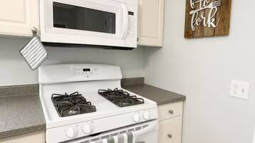 A kitchen with white cabinetry, a white microwave, a stove with four burners, and a wooden sign on the wall.