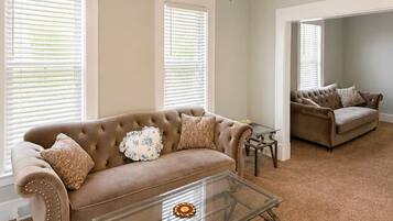 A living room with a brown sofa, a glass coffee table, and a ceiling fan.