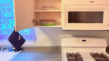 Una cocina con gabinetes blancos, microondas, estufa a gas y un cajón con utensilios.