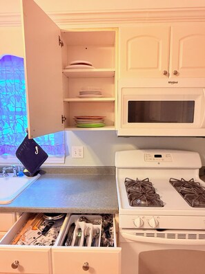 A kitchen with white cabinets, a microwave, a gas stove, and a drawer with utensils.