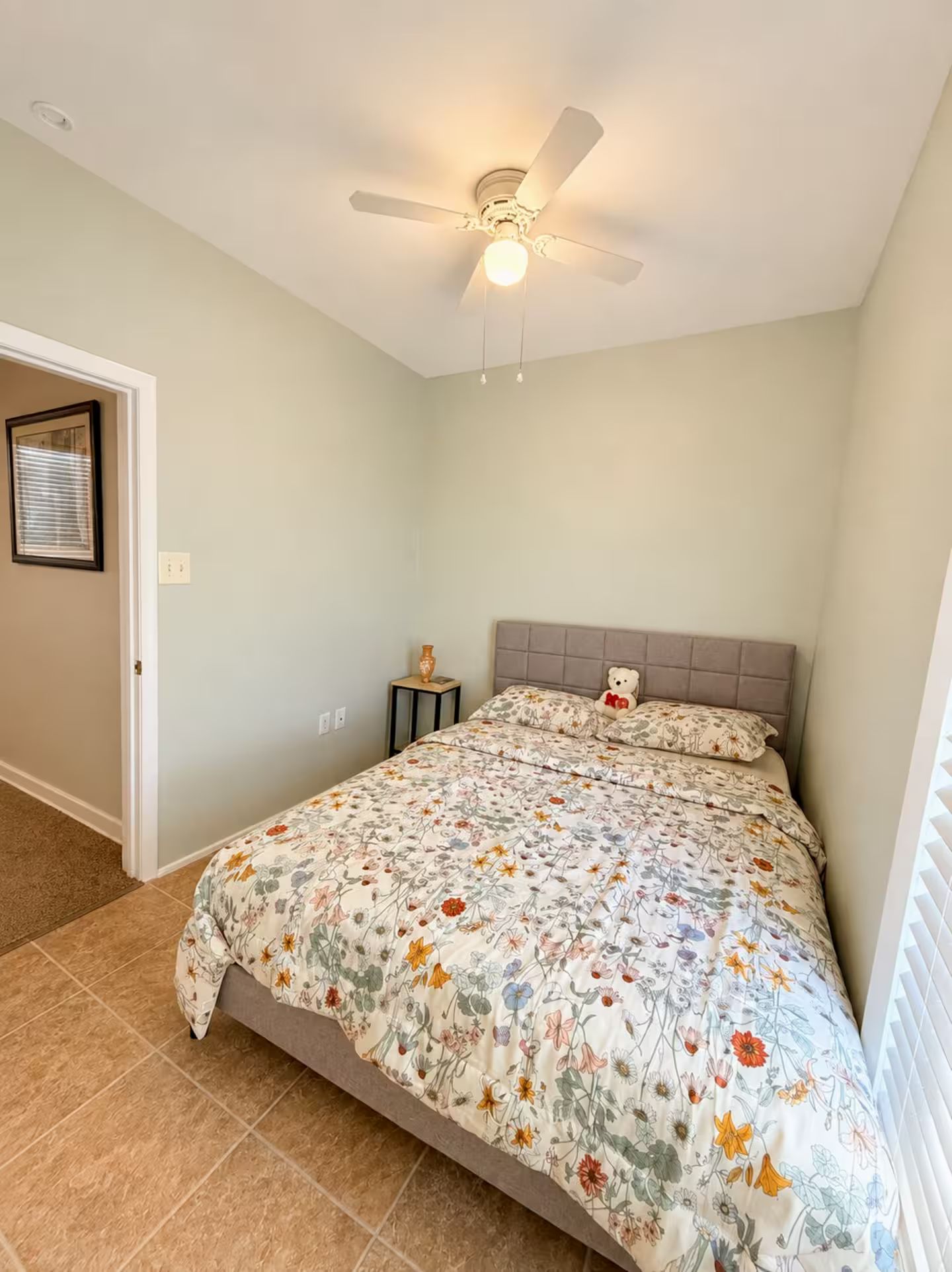 A bedroom with a bed, a ceiling fan, a nightstand, and a window with blinds.