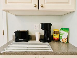 A kitchen counter with a toaster, a coffee maker, a jar of coffee creamer, and a bag of coffee grounds.