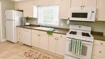 A kitchen with white cabinets, a refrigerator, a stove, a microwave, and a window with a curtain.