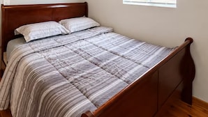 Ein Schlafzimmer mit einem hölzernen Bett, einem Deckenventilator, einem Fenster mit Jalousien und einer wandmontierten Lampe.