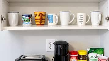 Una encimera de cocina con un tostador, una cafetera y varias tazas y recipientes para café.