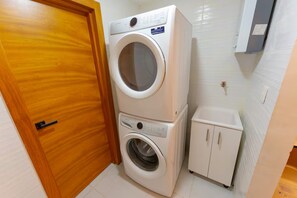 A laundry room with a stacked washer and dryer, a small cabinet, and a wooden door. - Modern Piantini Stay Prime Location + Pool (Santo Domingo)