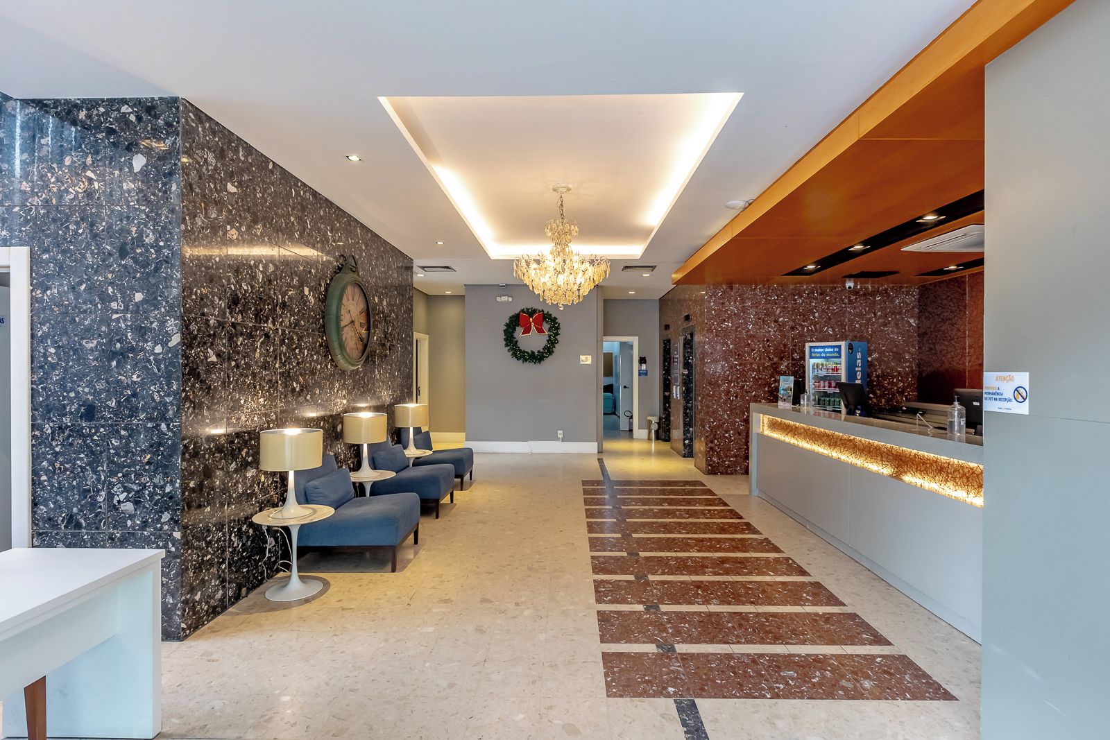 A hotel lobby with a reception desk, seating area, and a chandelier.