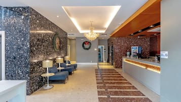 A hotel lobby with a reception desk, seating area, and a chandelier.