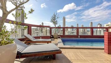 A rooftop terrace with a swimming pool, lounge chairs, and a view of the city skyline.