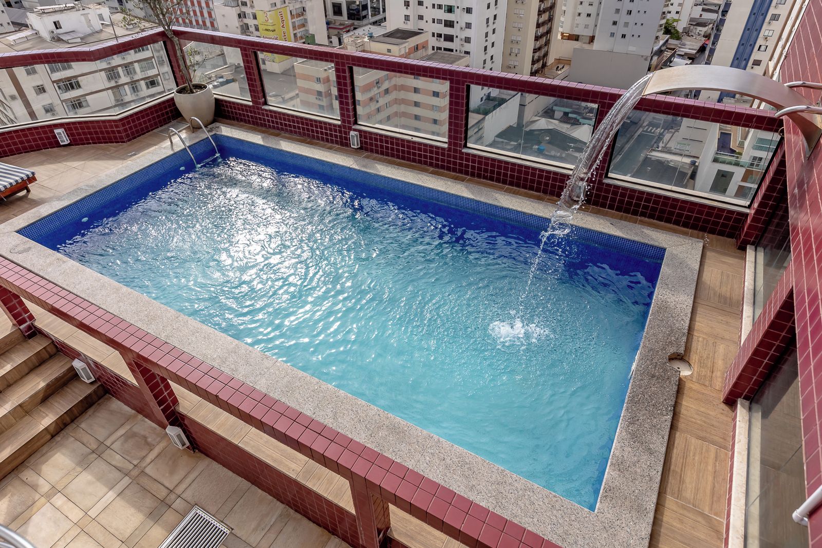 A rooftop swimming pool with a red-tiled edge, surrounded by a red-tiled balcony.