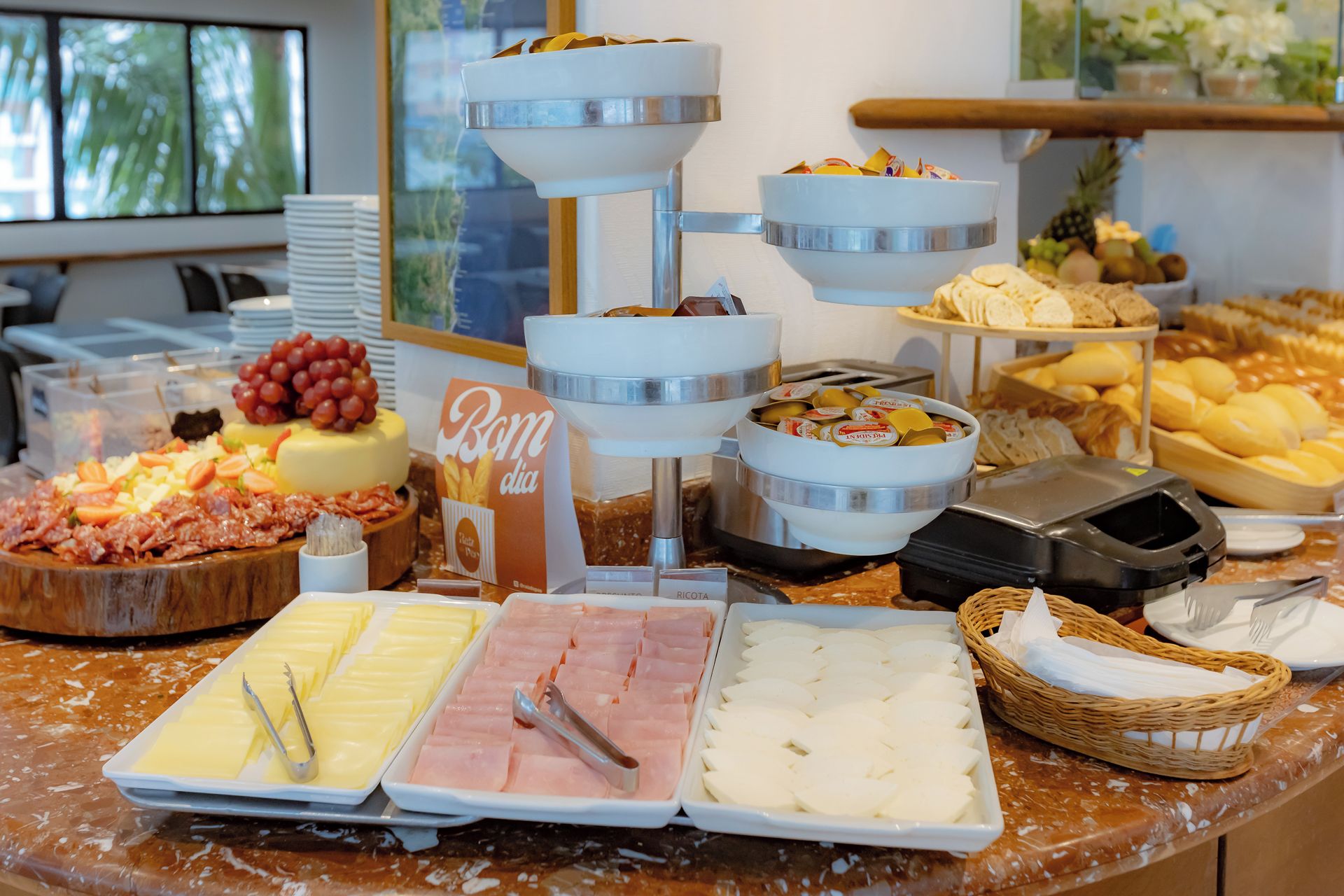 Un bufé con diversas opciones de comida, incluyendo queso, jamón y frutas.