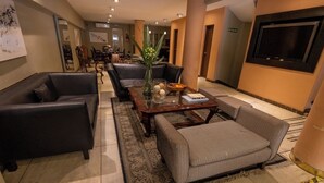 Um saguão de hotel com área de estar, incluindo sofás, poltronas, uma mesa de centro e um vaso decorativo.