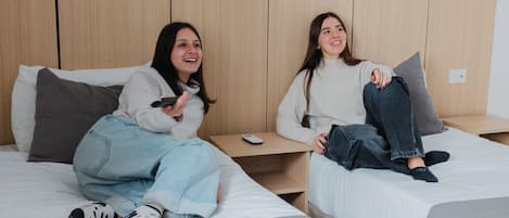 Two beds with wooden headboards, a bedside table with a remote control, and a wall-mounted light fixture.