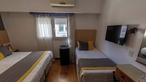 Quarto de hotel com duas camas, televisão, janela com cortinas e piso de madeira.