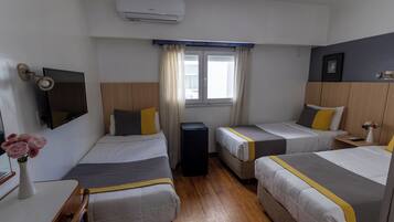 A hotel room with three beds, a TV, a window with curtains, and an air conditioning unit.