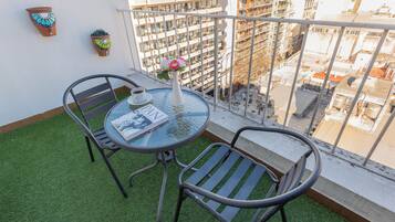 A balcony with a glass table, two chairs, a potted plant, and a magazine.