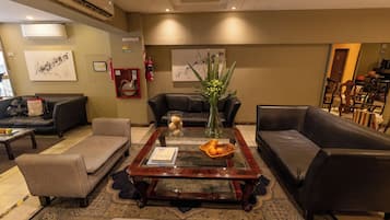 A hotel lobby with leather sofas, a coffee table with books and oranges, a vase with flowers, and a fire extinguisher.