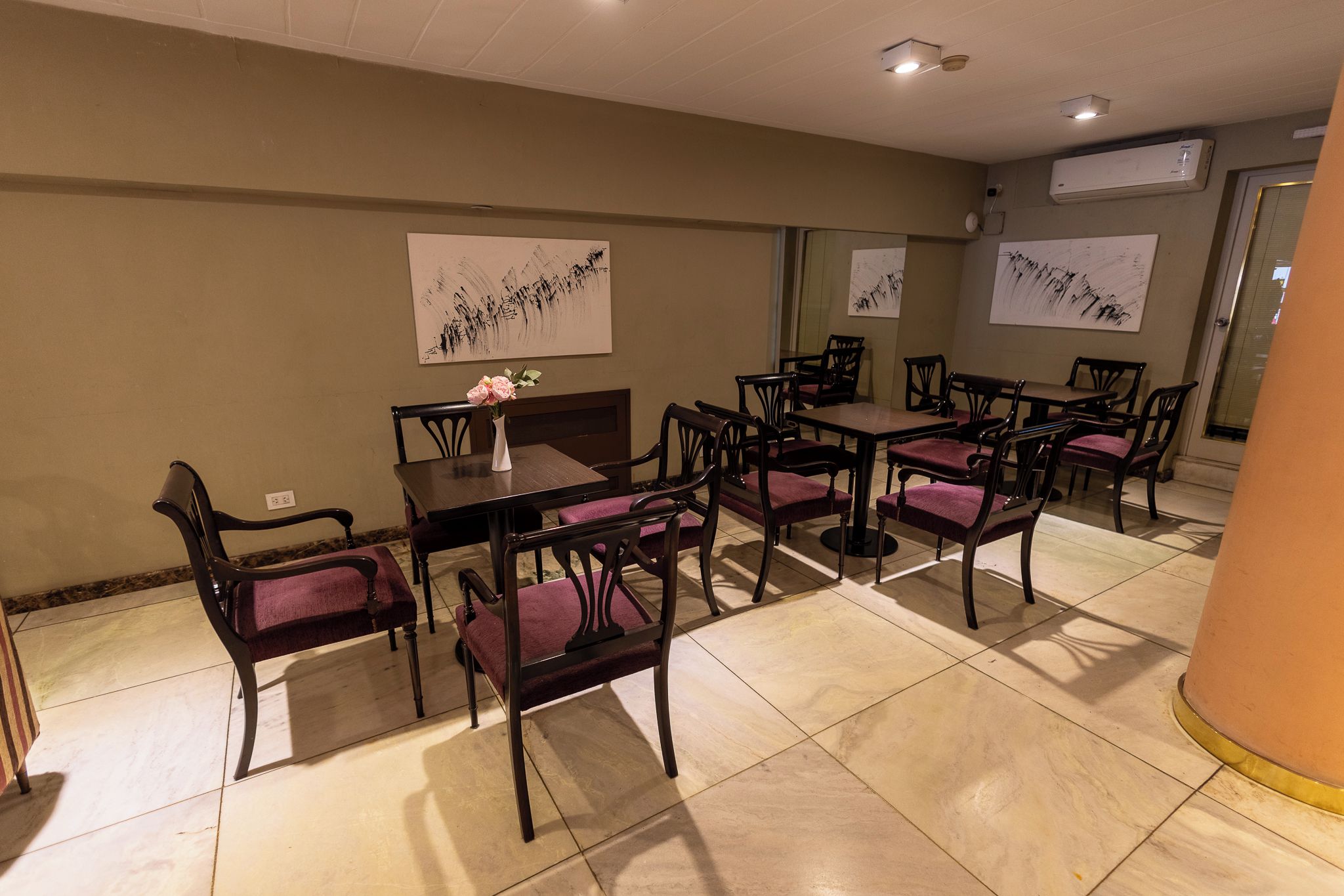 Un espace repas avec des tables et des chaises, des œuvres d’art accrochées aux murs et un appareil de climatisation.