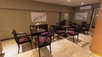 A dining area with tables and chairs, artwork on the walls, and an air conditioning unit.