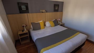 A hotel room with a bed, bedside tables, a nightstand, a wall-mounted light fixture, and framed pictures.