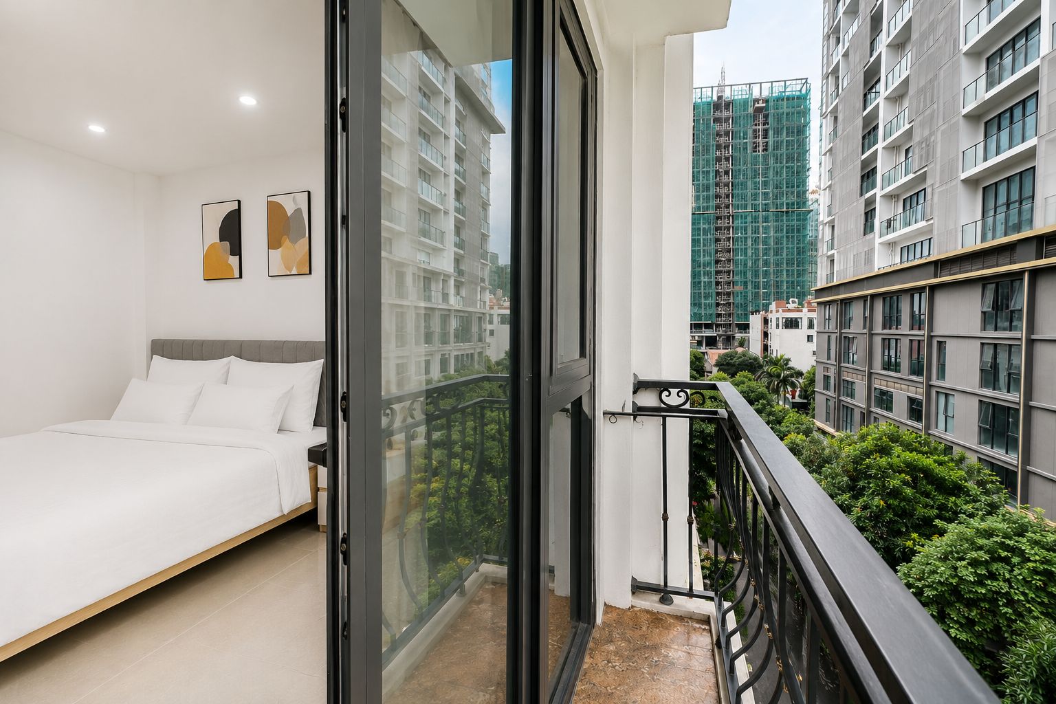 Un dormitorio moderno con cama, puerta de cristal que da a un balcón y vistas de edificios circundantes.