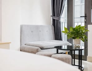 A grey armchair with a matching ottoman, a small round table with a potted plant, and a door with a curtain. - 200m to West Lake | Balcony Studio | Private Kitchen & In-unit Washer/Dryer (Hà Nội)