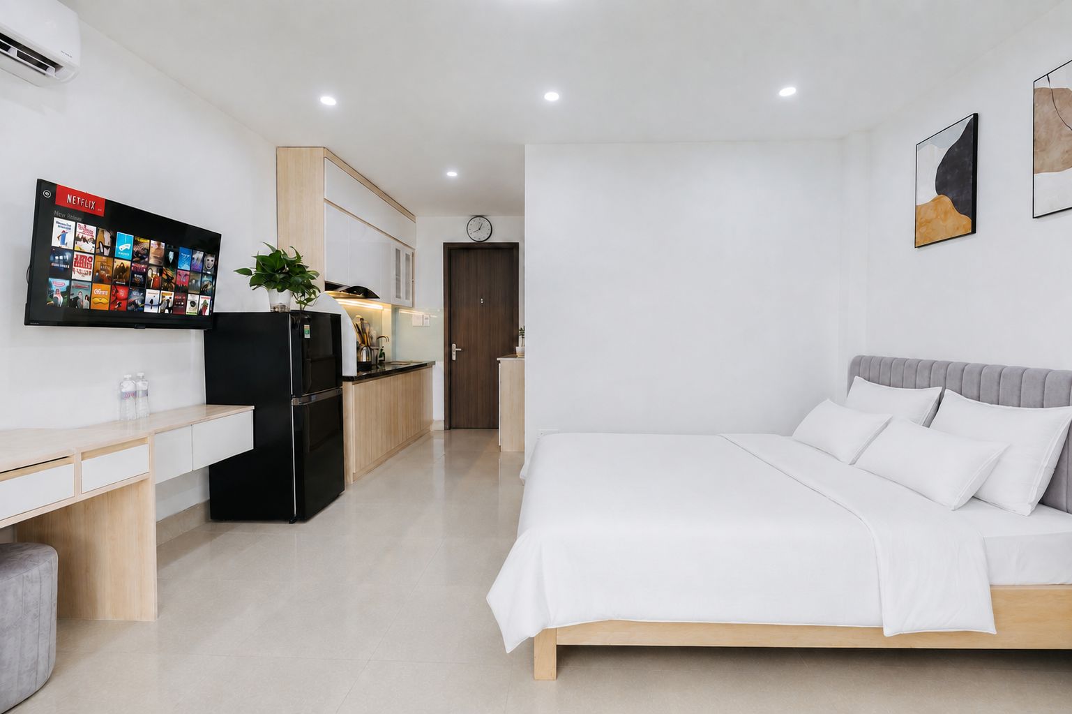 A modern hotel room with a bed, a desk, a refrigerator, a television, and a clock on the wall.
