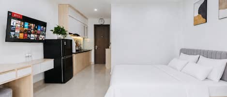 Habitación de hotel moderna con cama, escritorio, refrigerador, televisión y un reloj en la pared.