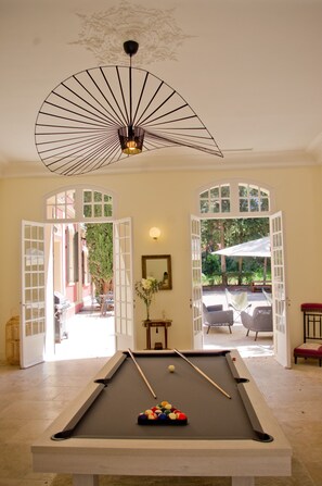 A pool table with balls, a ceiling fan, and a view of an outdoor area with chairs and a table. - Villa Aur a in 83220 (Le Pradet)