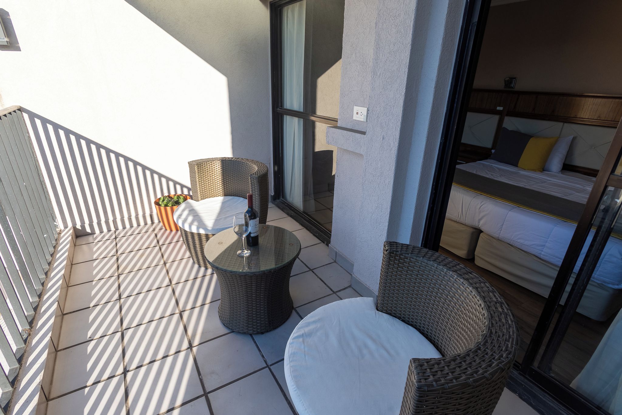 A balcony with wicker furniture, a glass door leading to a bedroom, and a potted plant.