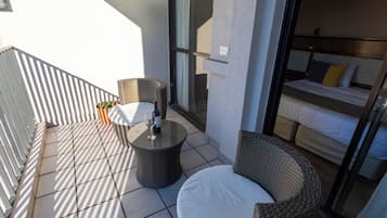 A balcony with wicker furniture, a glass door leading to a bedroom, and a potted plant.