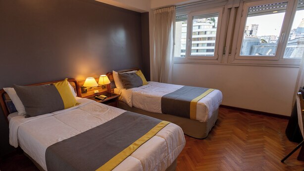 A hotel room with two beds, wooden flooring, a window with curtains, and a nightstand with lamps. - STAY HOTEL PLAZA SAN MARTIN (Buenos Aires)