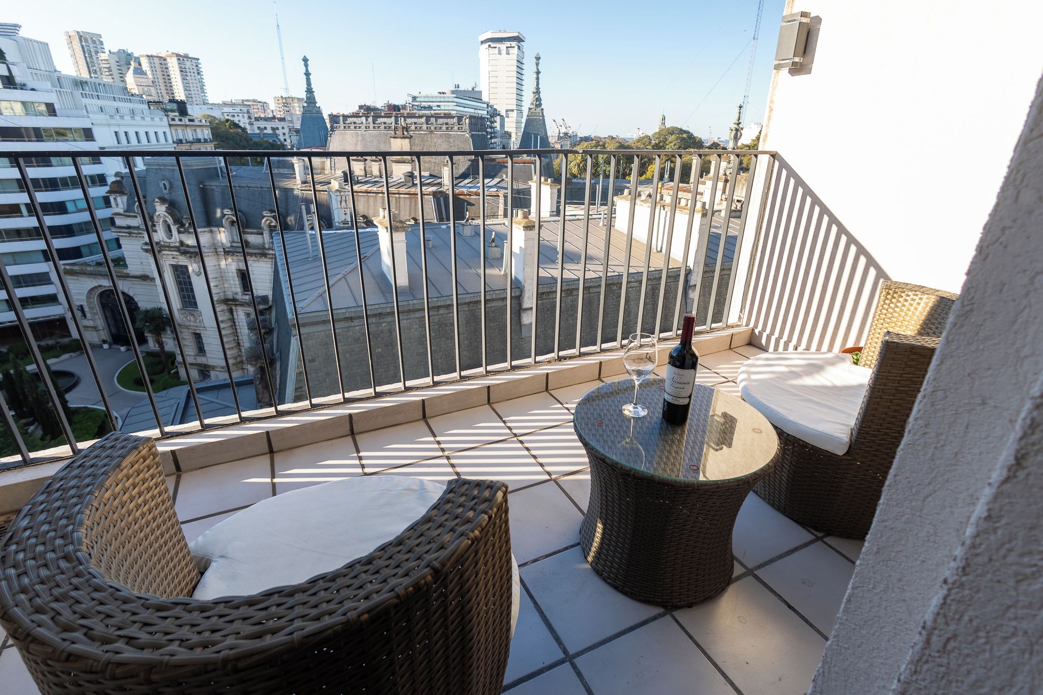 Ein Balkon mit Korbmöbeln, einem Tisch und einer Weinflasche.