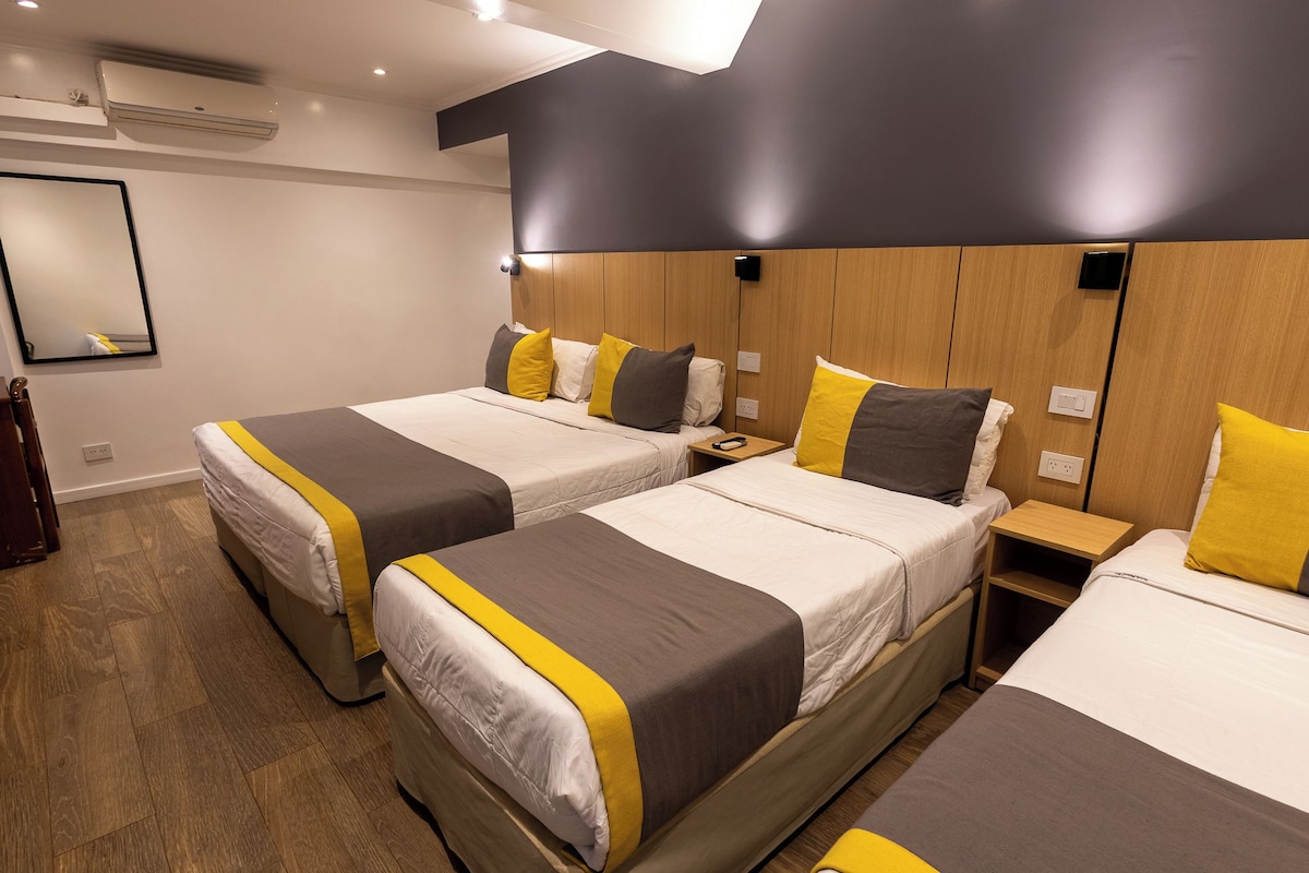 A hotel room with two beds, each with a wooden headboard, a bedside table, and a mirror.