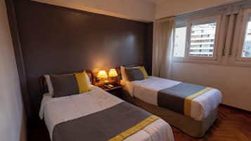 Habitación de hotel con dos camas, una mesita de noche con lámparas y una ventana con cortinas.