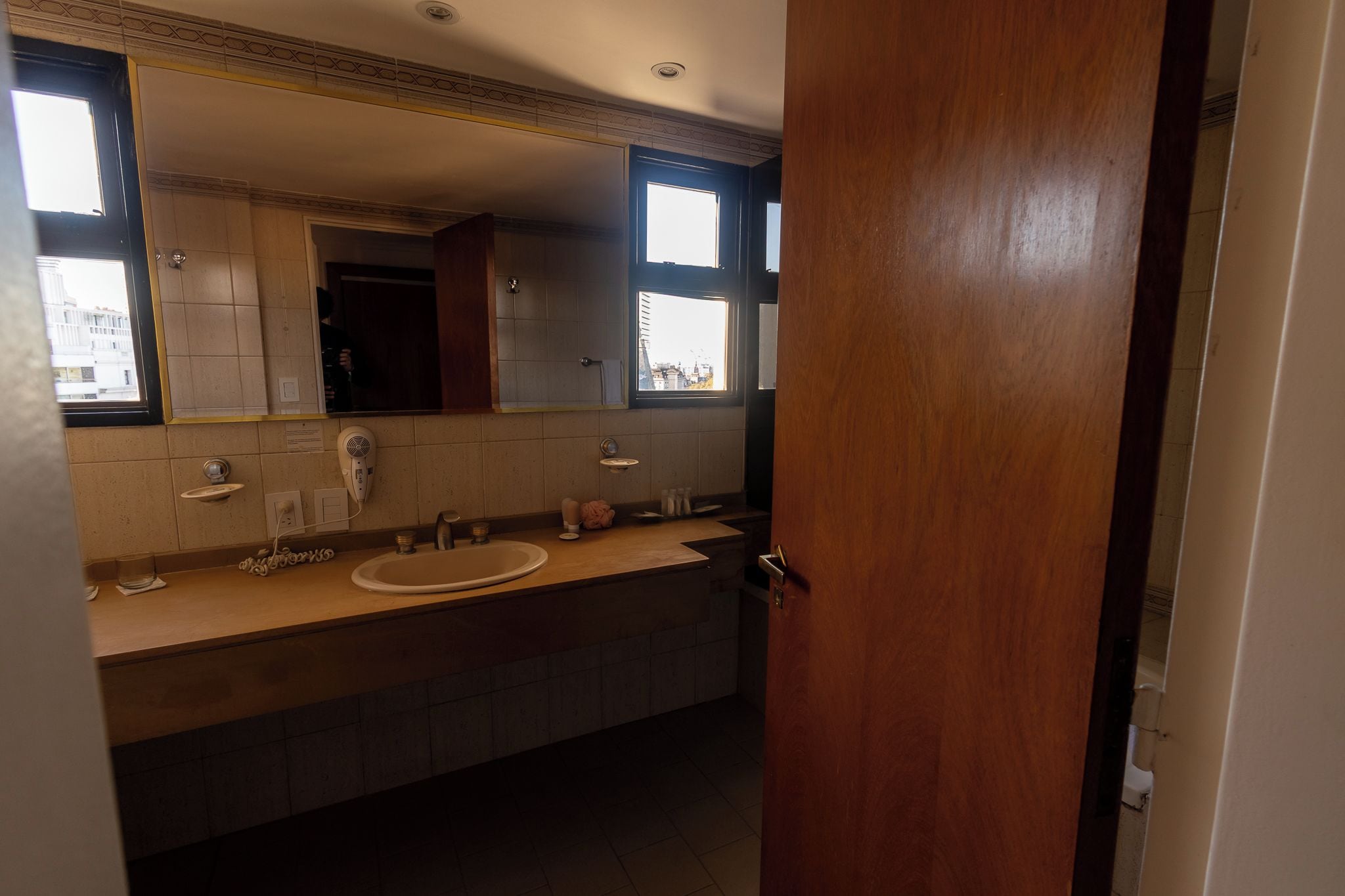 Ein Badezimmer mit einem Holzbadezimmerhocker, zwei Waschbecken, einem Spiegel und einem Fenster.