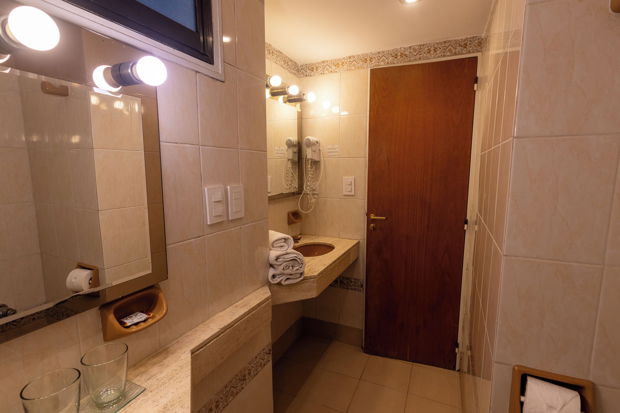 A bathroom with a sink, mirror, towel dispenser, and a door.