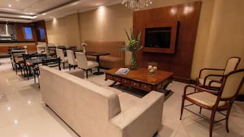 Un moderno vestíbulo de hotel con un sofá, zona de comedor y un televisor montado en la pared.