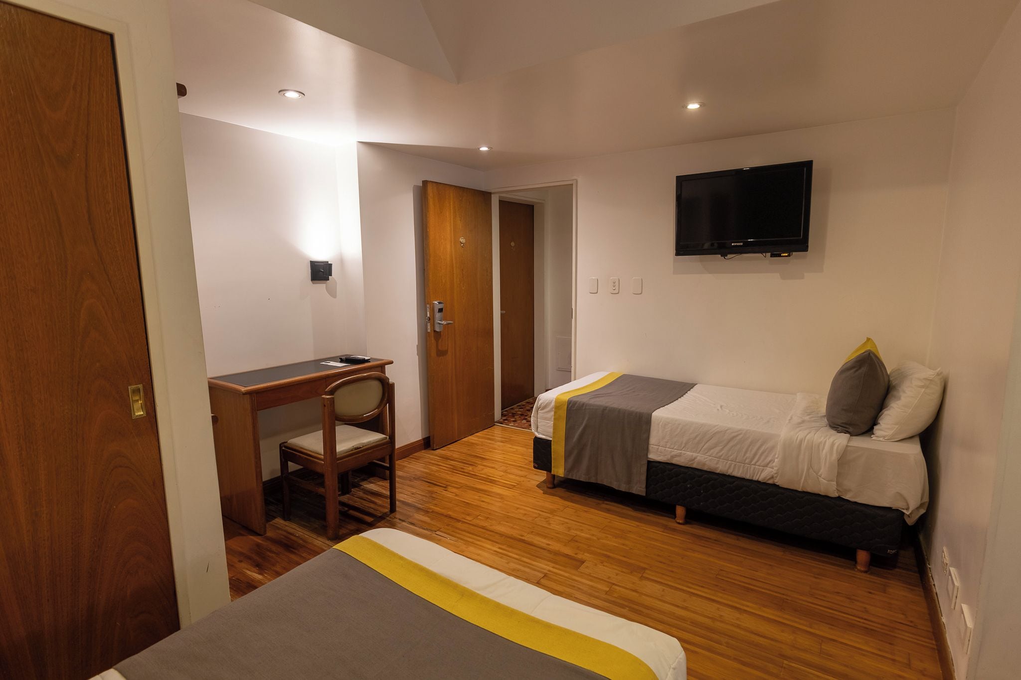 A hotel room with a desk, two beds, a TV, and a wooden floor.