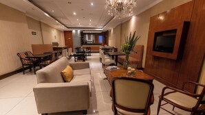 A hotel lobby with sofas, chairs, a dining area, a chandelier, and a TV mounted on the wall. - STAY HOTEL PLAZA SAN MARTIN (Buenos Aires)