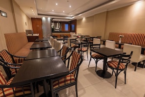 A restaurant with multiple tables and booths, some with striped upholstery, and a kitchen area in the background. - Stay Hotel Plaza San Martin (Buenos Aires)