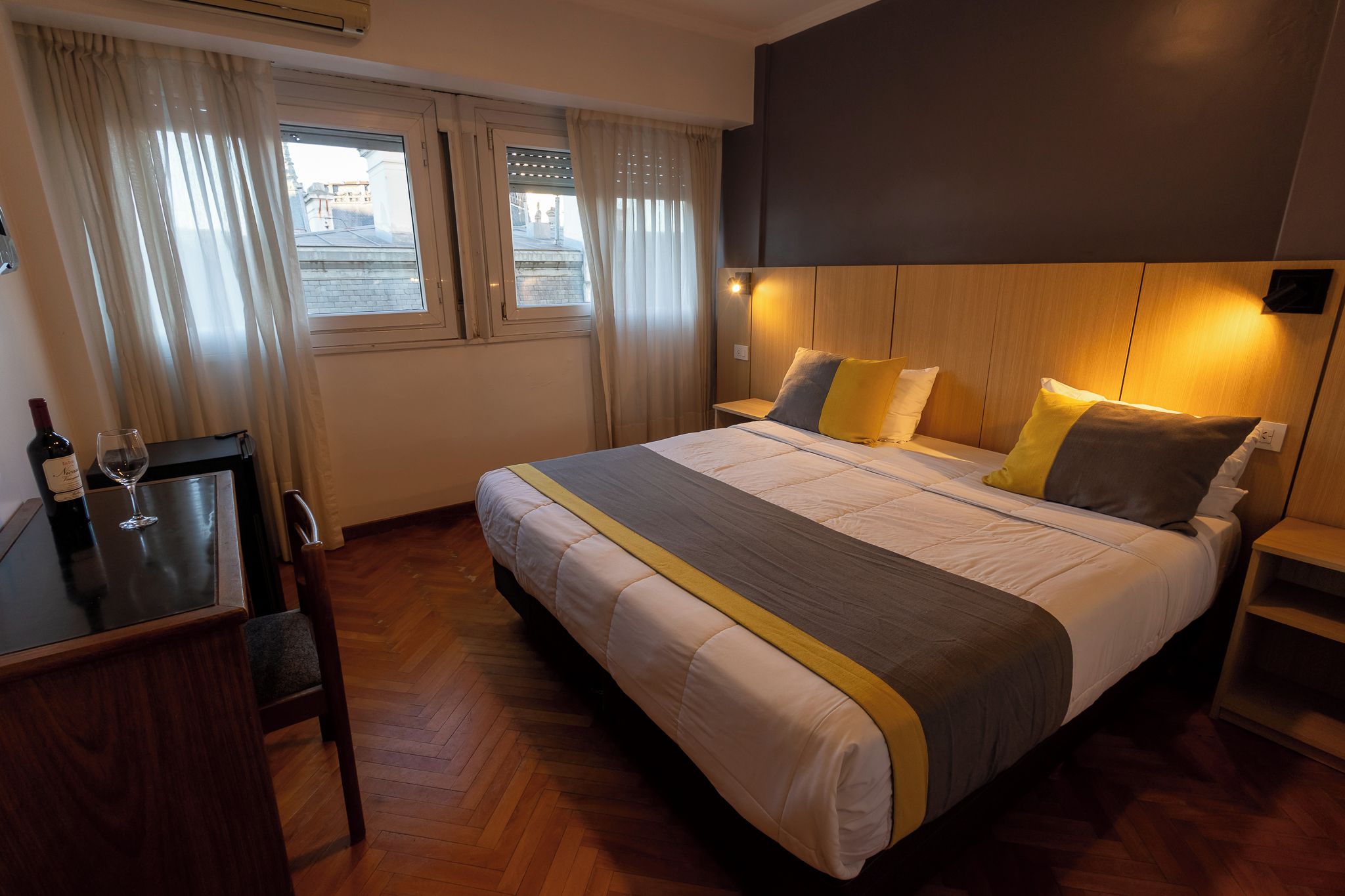 Una habitación de hotel con cama, mesita de noche y ventana con cortinas.