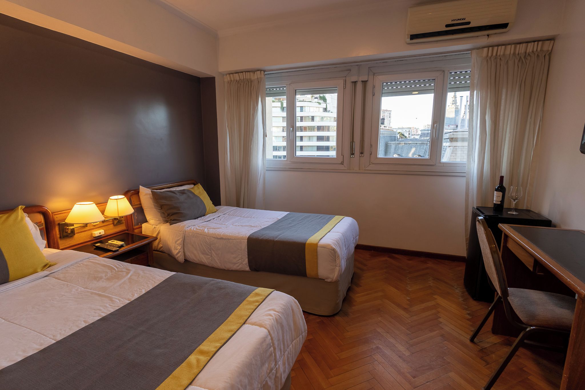 Habitación de hotel con dos camas, un escritorio, aire acondicionado y una ventana con cortinas.