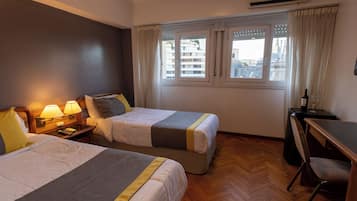 Habitación de hotel con dos camas, un escritorio, aire acondicionado y una ventana con cortinas.
