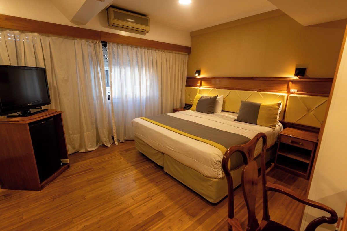 A hotel room with a bed, a TV, a desk, and a chair.