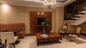 A modern living room with a wooden coffee table, a sofa, and two armchairs. A chandelier hangs from the ceiling, and a television is mounted on the wall. - STAY HOTEL PLAZA SAN MARTIN (Buenos Aires)