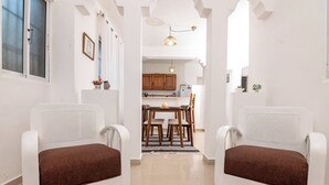A modern interior with two white armchairs, a dining table, and a kitchen area. - Puerto Plata | 2BR | Jacuzzi | Terrace | Modern & Central (Puerto Plata)