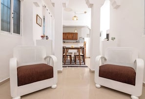 Een modern interieur met twee witte fauteuils, een eettafel en een keukenhoek.
