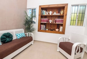 Une pièce avec un canapé blanc, un fauteuil blanc, une bibliothèque en bois et une plante en pot.
