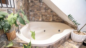 A spa area with a large bathtub, stone walls, and various potted plants. - Puerto Plata | 2BR | Jacuzzi | Terrace | Modern & Central (Puerto Plata)
